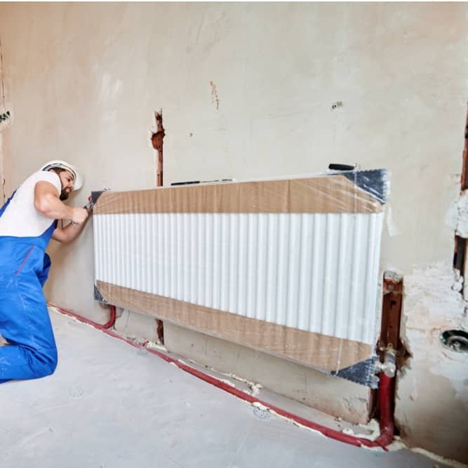 Plombier installant un radiateur de chauffage central dans un logement à Charleroi