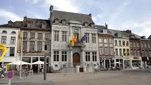 Rue pavée à Ath avec un plombier en action, enseigne typique derrière lui et maisons traditionnelles en briques.