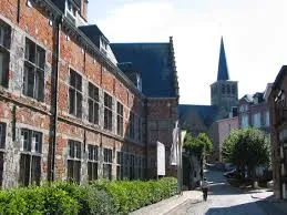 Vue d'une rue pavée de Lessines avec enseigne Plombier Lessines en arrière-plan et bâtiments typiques en briques.